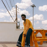 Editorial image of plunge kaftan tunic in golden turmeric tones, photographed against minimal coastal architecture