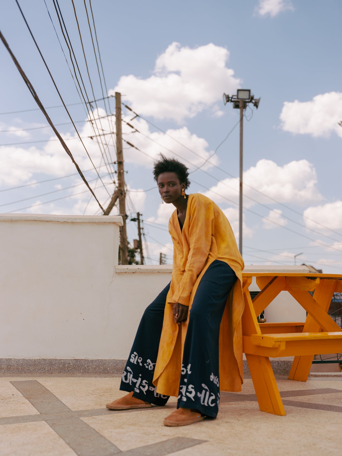 Editorial image of plunge kaftan tunic in golden turmeric tones, photographed against minimal coastal architecture