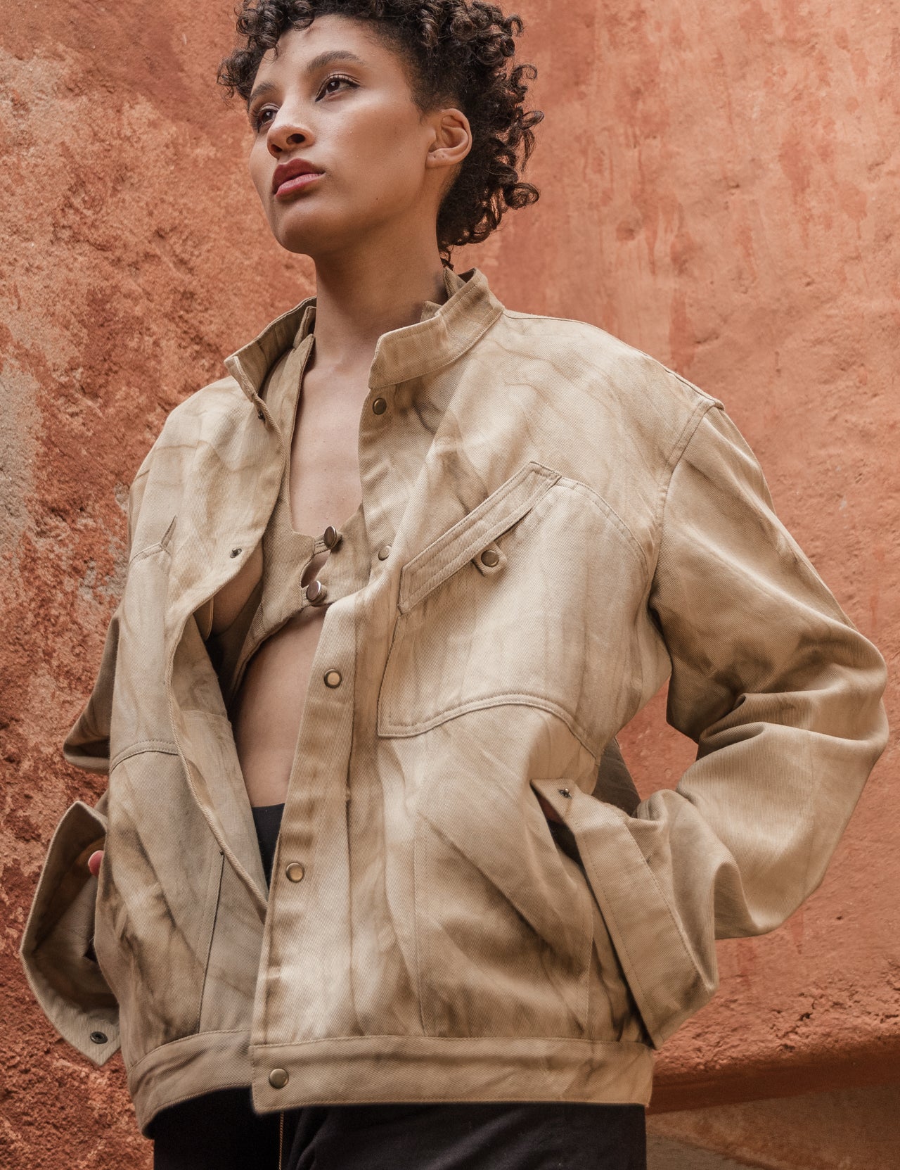 Model wearing marbled safari jacket in natural red-soil tie-dye against a terracotta wall
