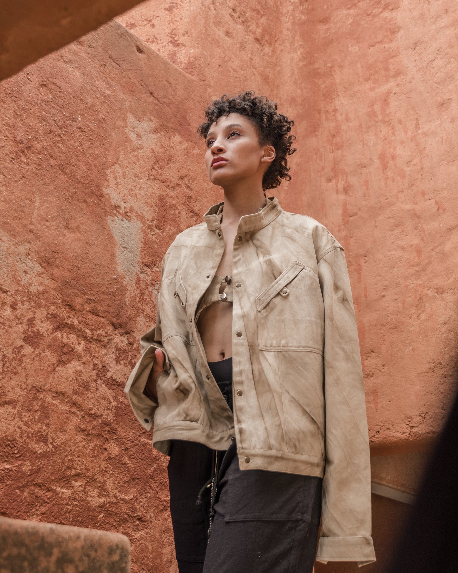 Model wearing marbled safari jacket in natural ochre tie-dye against a terracotta wall