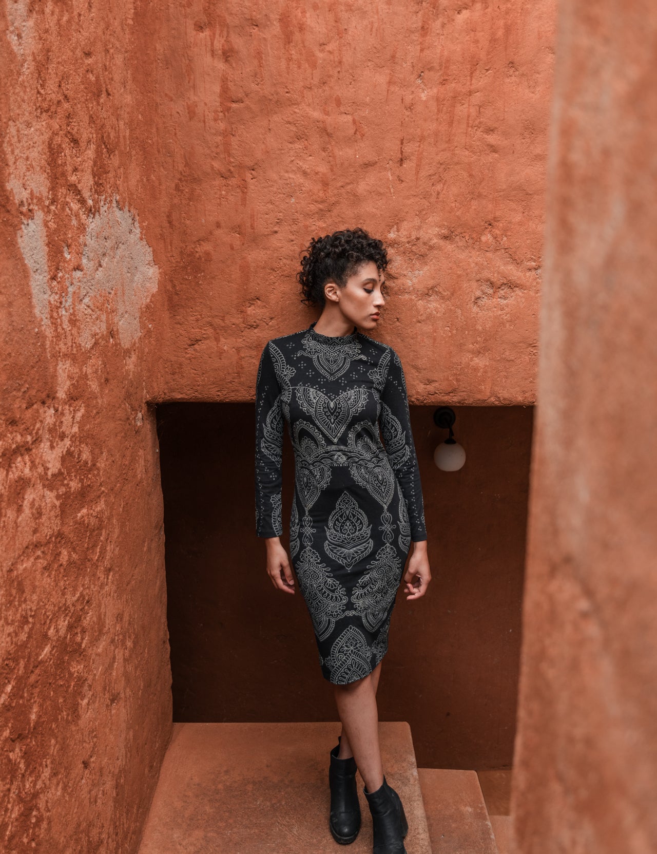 Model in black form-fitting Mehendi Cocktail Dress with long sleeves, featuring digitally engineered laser-engraved blockprint design in natural cotton jersey by LilaBare.