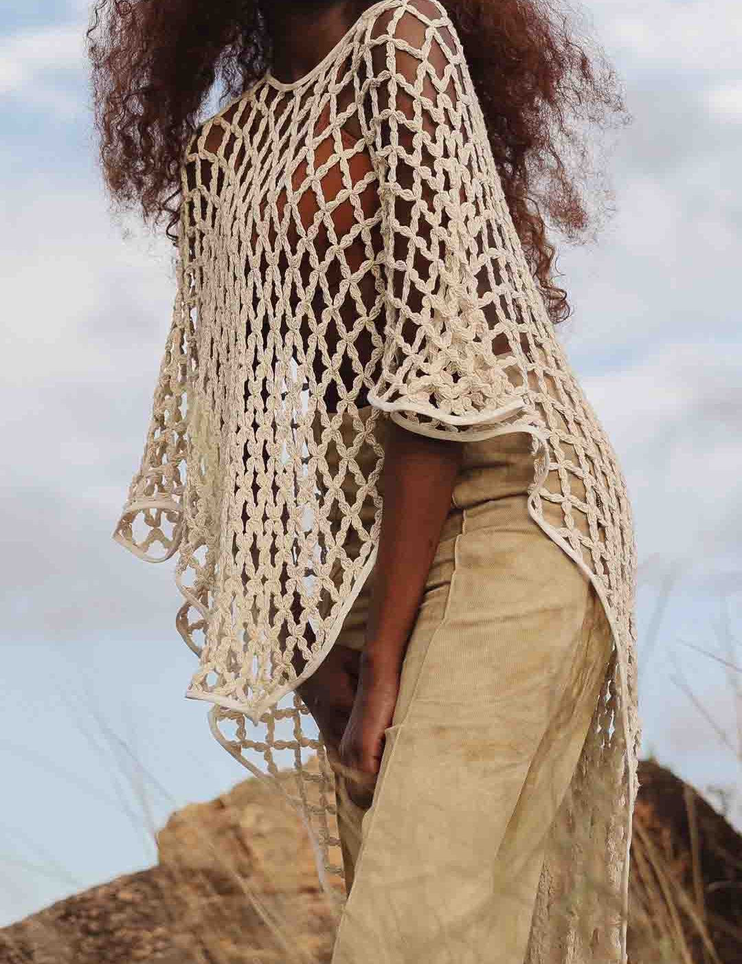 Side view of LilaBare model wearing hand-crocheted cotton bolero mid-movement, capturing fishnet crochet and fluid silhouette