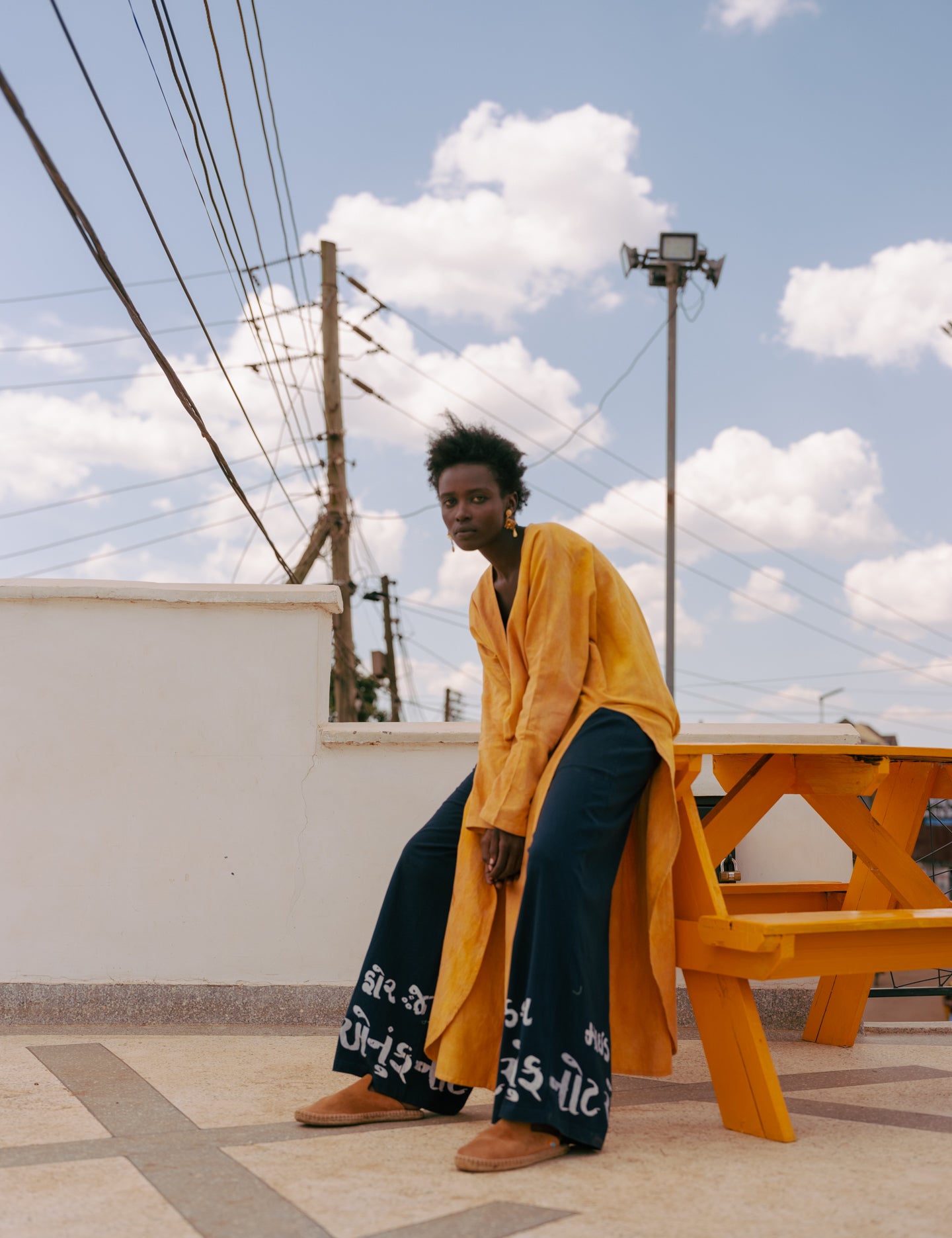 Editorial image of plunge kaftan tunic in golden turmeric tones, photographed against minimal coastal architecture
