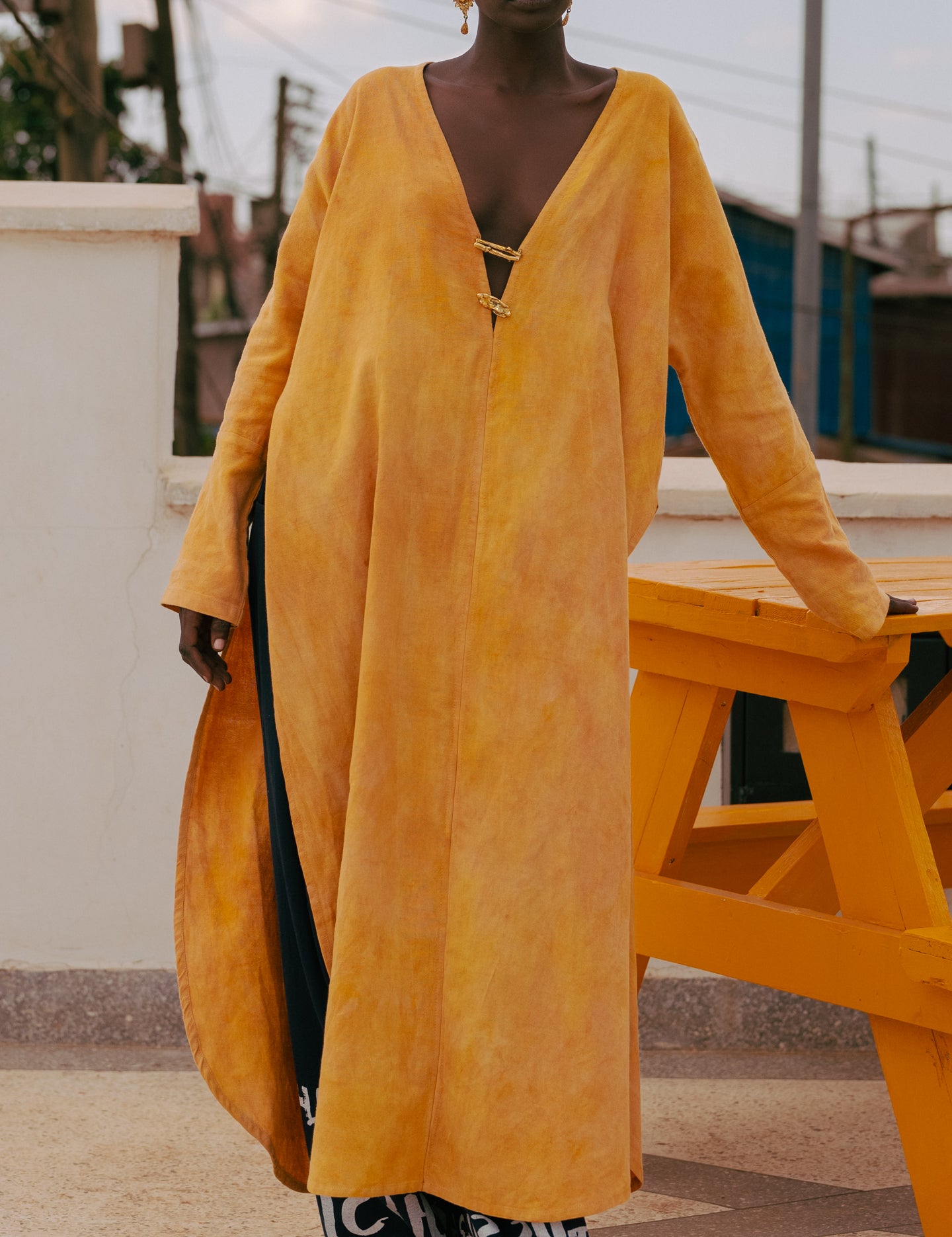 Model wearing LilaBare’s plunge kaftan tunic, hand-dyed with turmeric and red soil, featuring brass closures and waist-level slits