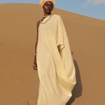 Model wearing LilaBare’s One Shoulder Sari Dress in undyed handloom cotton, walking barefoot in golden desert sand at sunrise.