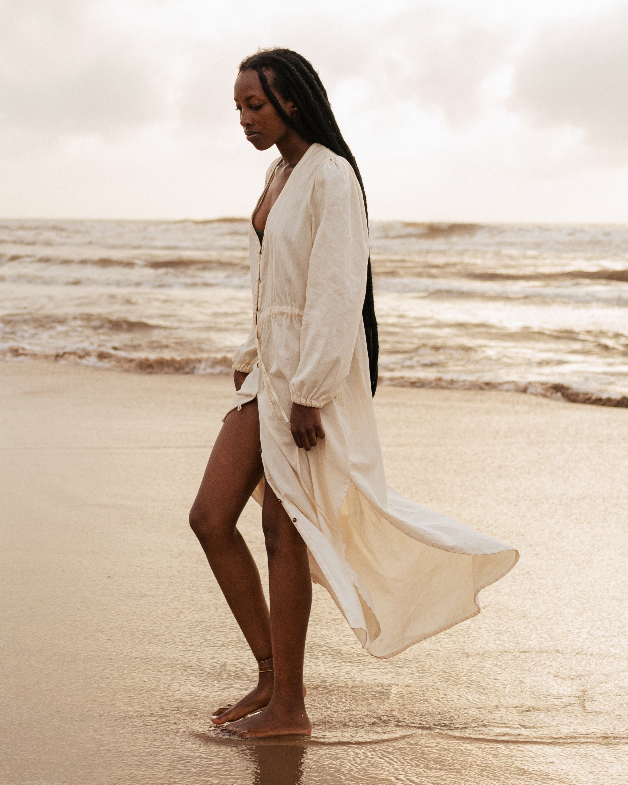 Woman walking barefoot along the shore in flowing LilaBare Louise Cape Dress made of handwoven cotton