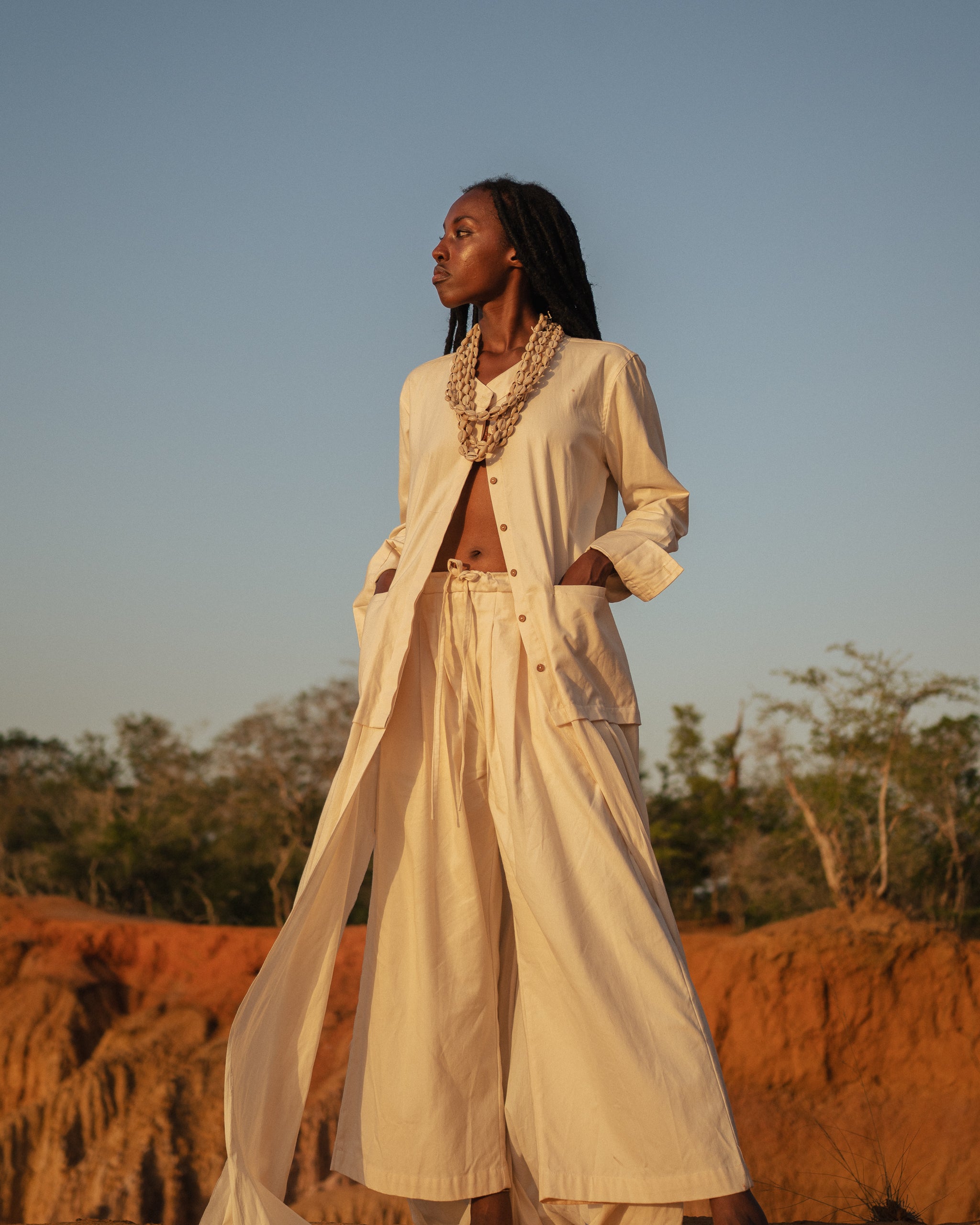 Model wears the Shakti Shirt and wide-leg pants in a sunlit natural setting, showcasing relaxed silhouette and gender-fluid style.