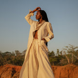 Model wears the Shakti Shirt and wide-leg pants in a sunlit natural setting, showcasing relaxed silhouette and gender-fluid style.