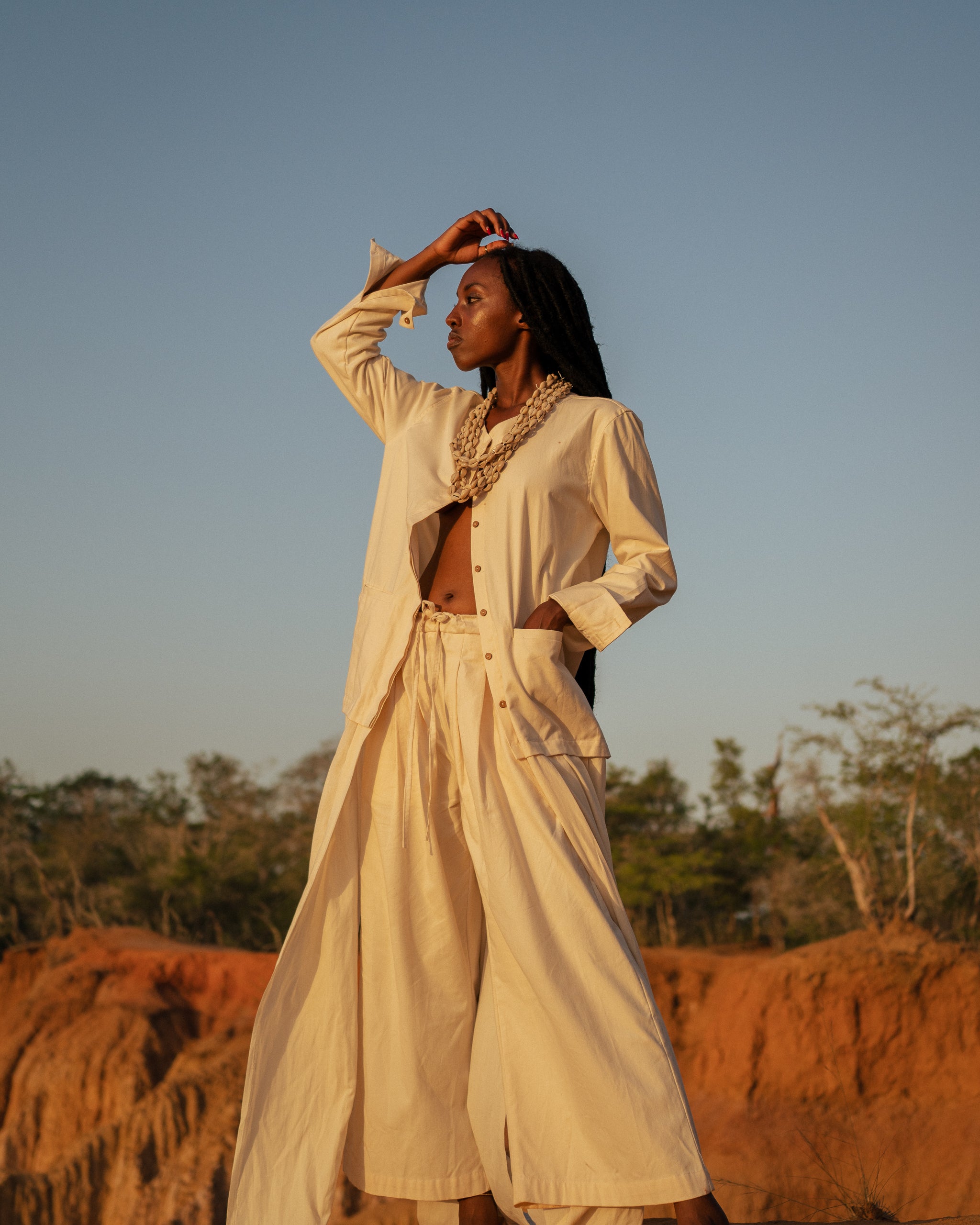 Model wears the Shakti Shirt and wide-leg pants in a sunlit natural setting, showcasing relaxed silhouette and gender-fluid style.