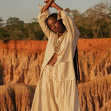 Model wears the Shakti Shirt and wide-leg pants in a sunlit natural setting, showcasing relaxed silhouette and gender-fluid style.