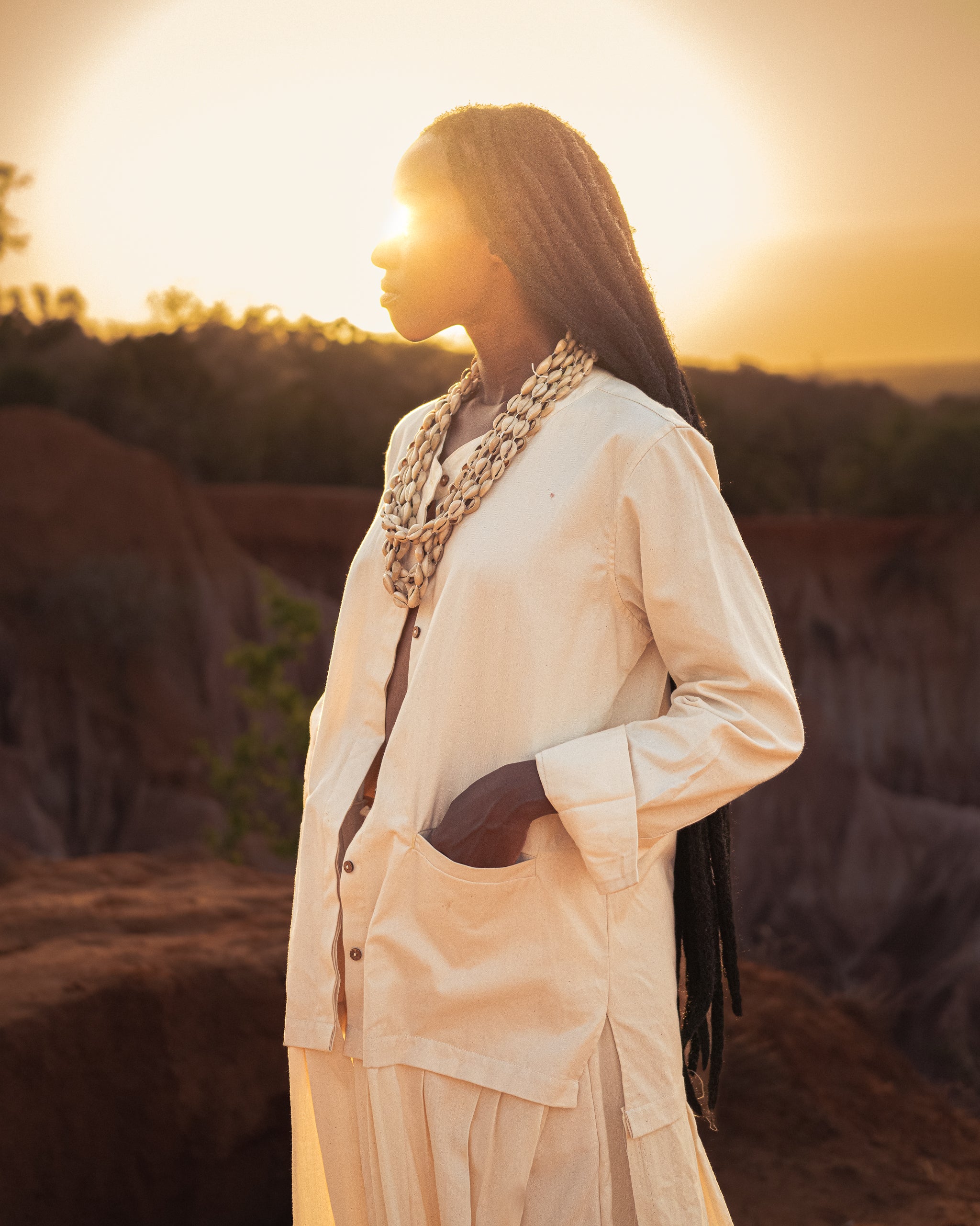 Close up side view of model wears the Shakti Shirt and wide-leg pants in a sunlit natural setting, showcasing relaxed silhouette and gender-fluid style.