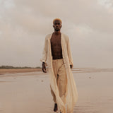 Model wears the Shakti Shirt and wide-leg pants in a sunlit natural setting, showcasing relaxed silhouette and gender-fluid style.