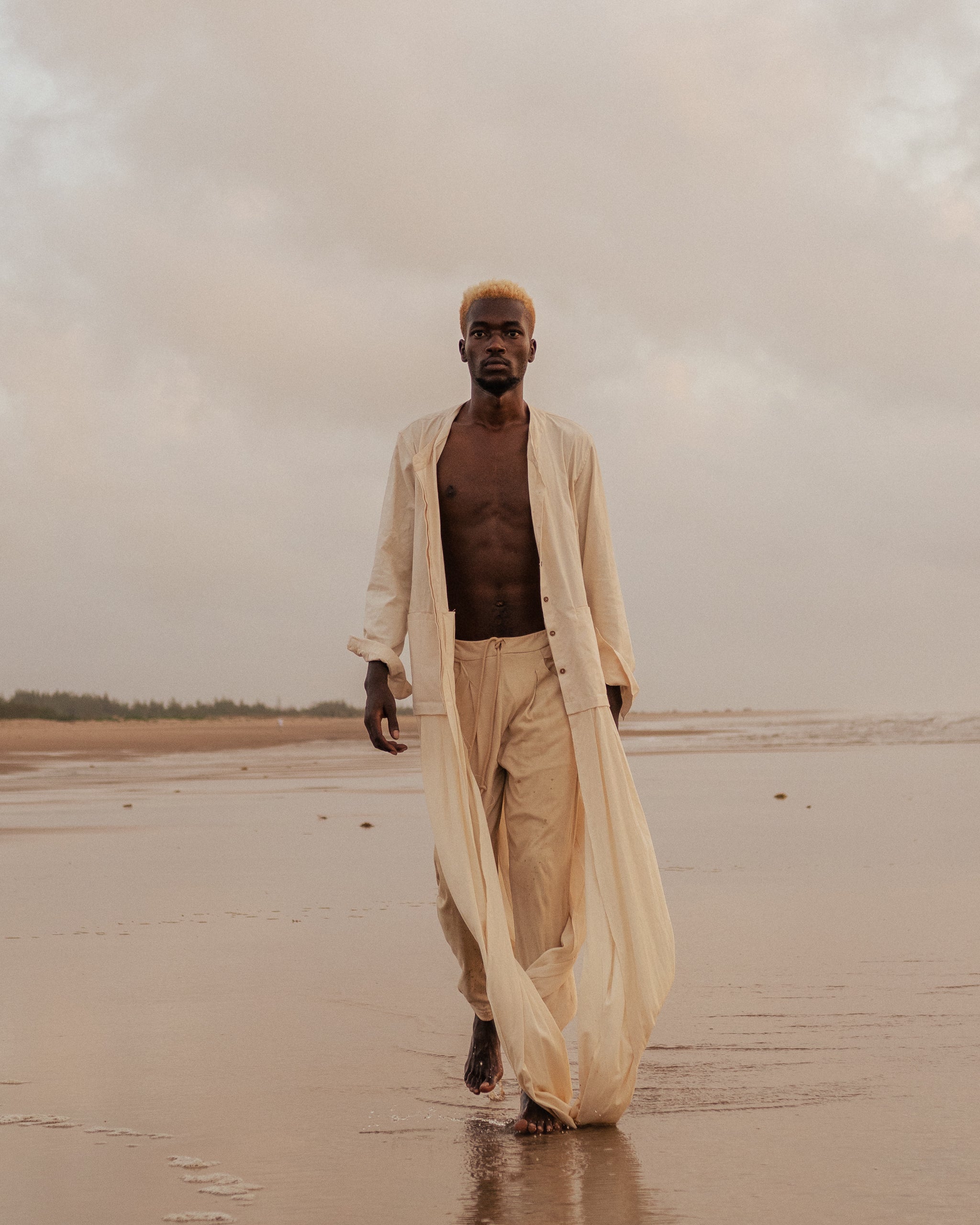 Model wears the Shakti Shirt and wide-leg pants in a sunlit natural setting, showcasing relaxed silhouette and gender-fluid style.